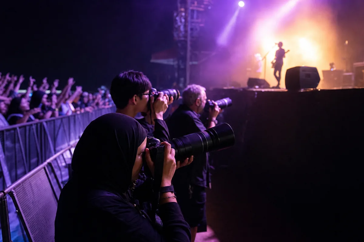 Accredited photographers shooting from the photo pit below a concert stage under coloured stage lights