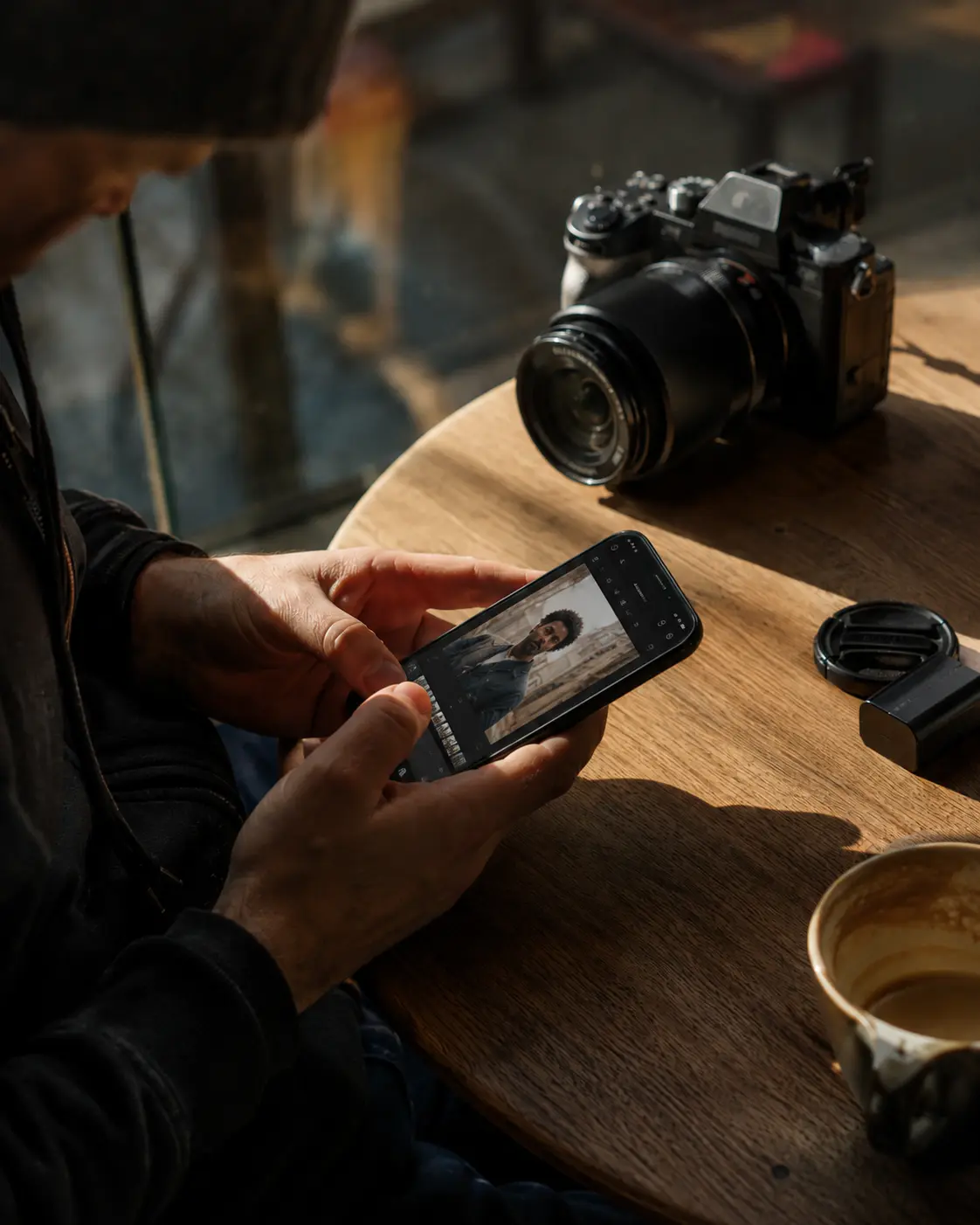 Photographer editing photos on a phone at a table straight after a shoot, camera and lens beside them