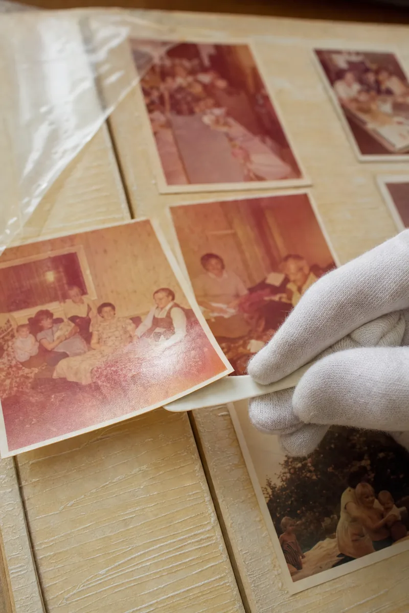 Gloved hand easing a faded 1970s colour print away from a yellowed self-adhesive album page with a thin plastic spatula